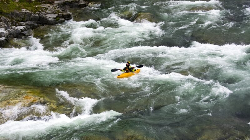 Kayakiste en kayak jaune naviguant dans des rapides d’une rivière de montagne.