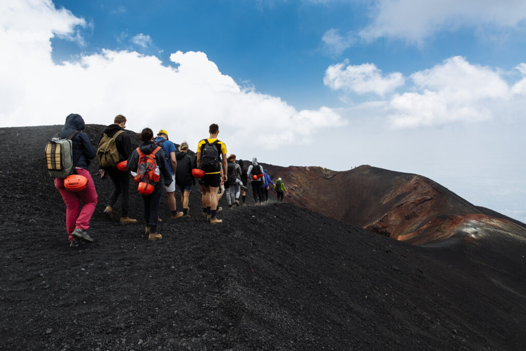 "Randonneurs en file indienne gravissant un sentier volcanique noir sous un ciel bleu, illustrant l’exploration du volcan Kilauea à Hawaï"