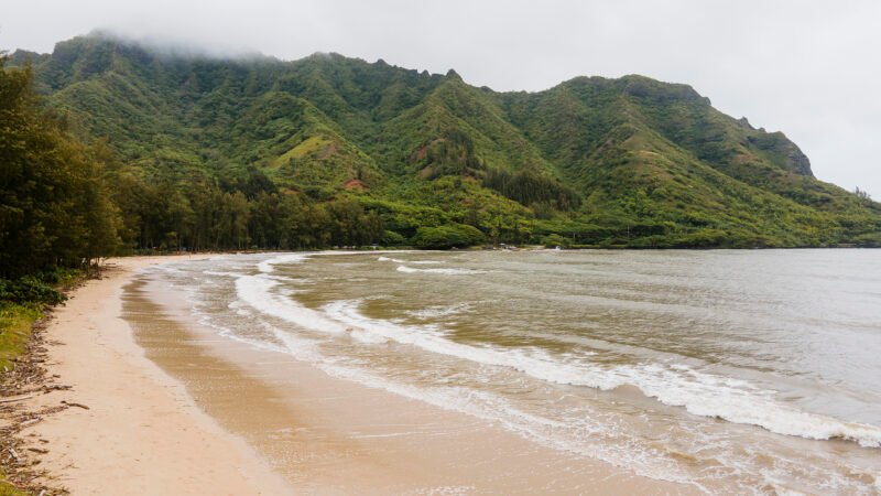 Plage de Hanalei Bay bordée d’une mer calme et de montagnes verdoyantes sous un ciel nuageux, sur l’île de Kauai à Hawaii.