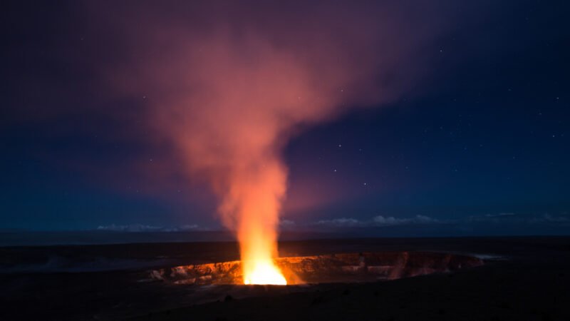 Éruption nocturne du cratère Halemaʻumaʻu au sommet du Kilauea, avec une colonne de lave incandescente illuminant le ciel étoilé