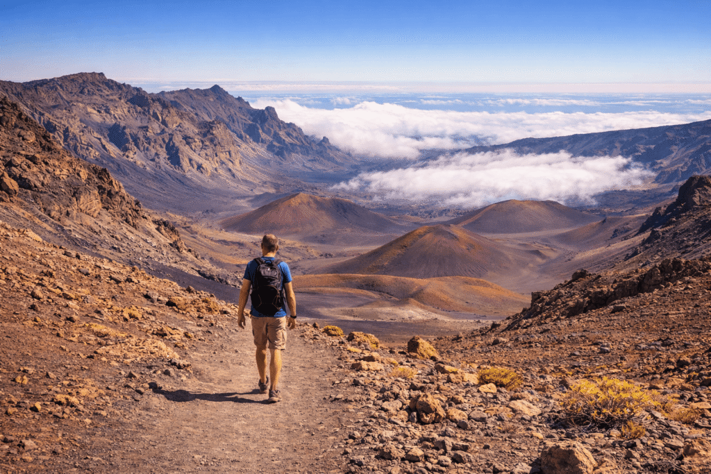 Randonneur progressant sur le Sliding Sands Trail, l’un des sentiers les plus célèbres du cratère Haleakalā, offrant une immersion totale au cœur de la caldeira volcanique.