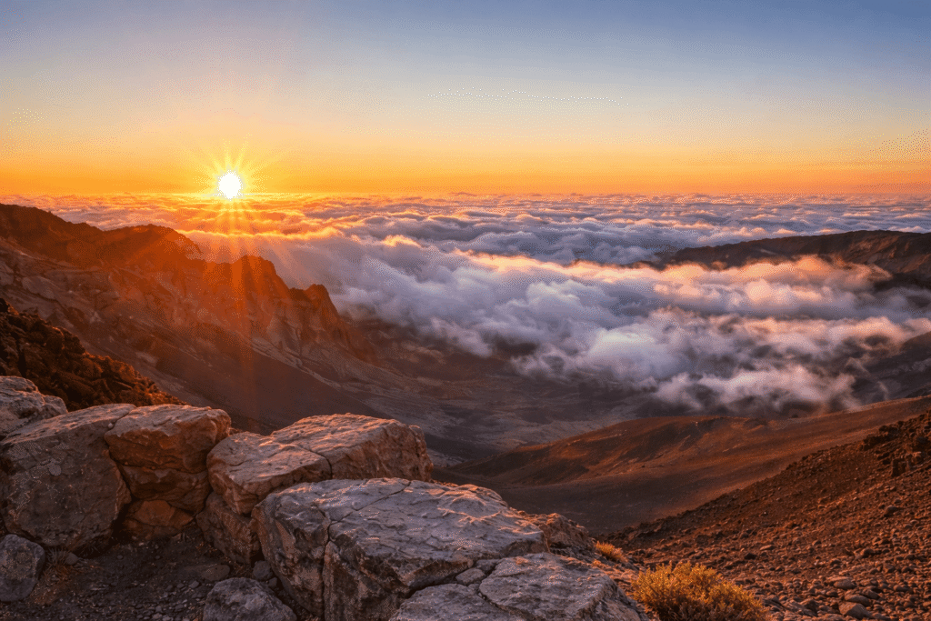 Lever de soleil magique au sommet du Haleakalā, offrant une vue saisissante au-dessus d’une mer de nuages, l’une des expériences les plus emblématiques du parc national de Haleakalā à Maui.