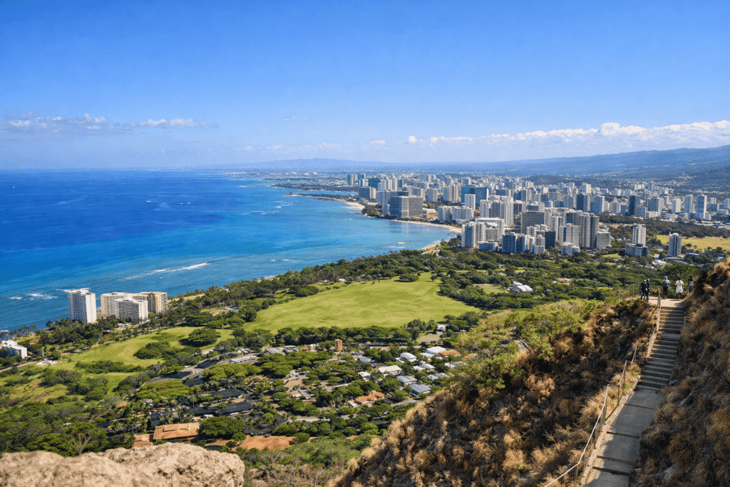 Vue large depuis le sommet de Diamond Head orientée vers l’intérieur de l’île, avec les quartiers urbains de Honolulu, les axes routiers et la plaine côtière visibles.