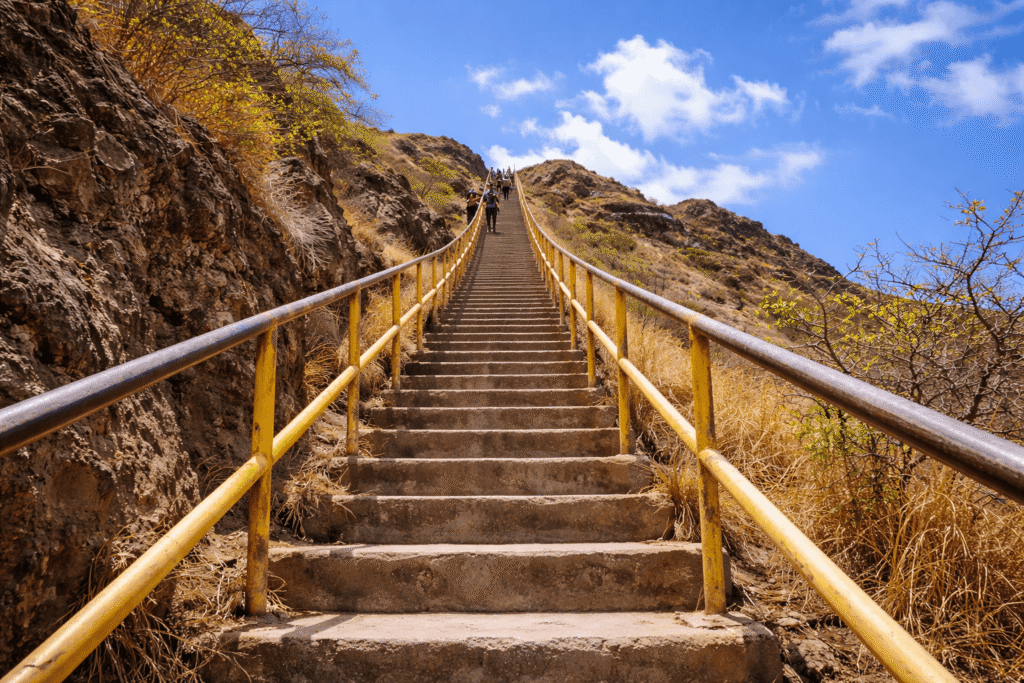 Vue en contre-plongée des escaliers raides du Diamond Head Trail, avec rambardes métalliques, roche volcanique et ciel visible au sommet, illustrant l’effort final de l’ascension.