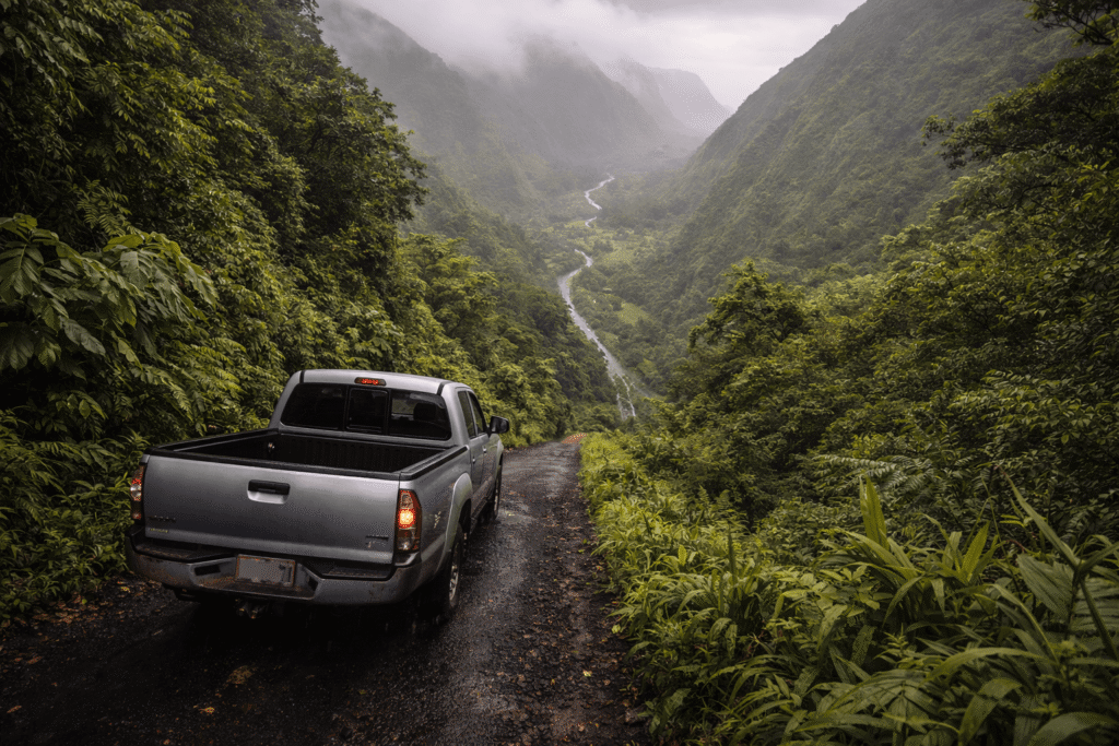 Véhicule 4x4 descendant une route très raide et étroite au cœur d’une végétation tropicale dense dans la vallée de Waipiʻo à Hawaï, dans une atmosphère brumeuse.