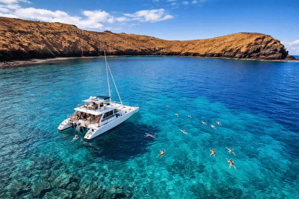 Catamaran d'excursion blanc ancré dans les eaux calmes et turquoise à l'intérieur du cratère de Molokini avec des snorkeleurs dans l'eau