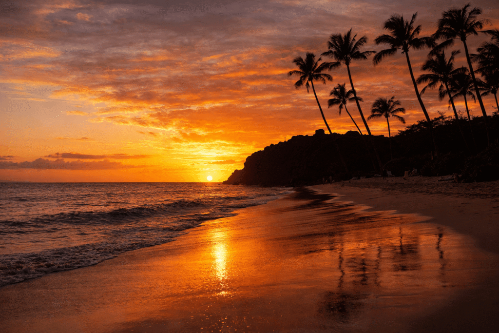 Coucher de soleil aux teintes orangées sur Kaanapali Beach avec Black Rock et des palmiers en silhouette, Maui