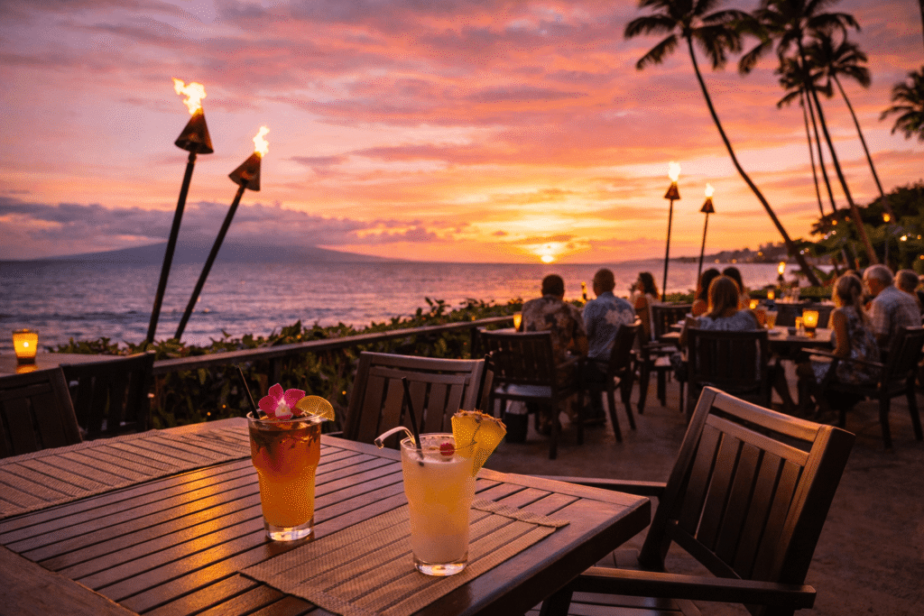 Terrasse de restaurant en bord de mer à Kihei au coucher du soleil avec torches tiki et cocktails tropicaux