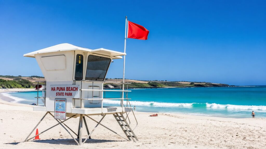 Tour de surveillance des lifeguards arborant un drapeau rouge sur la plage de sable blanc de Hapuna Beach.