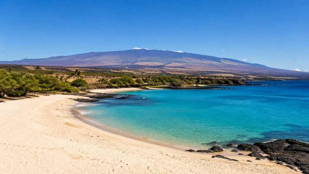 Panorama de la côte Kohala depuis Hapuna Beach avec sable blanc, formations de lave et le volcan Mauna Kea en arrière-plan.