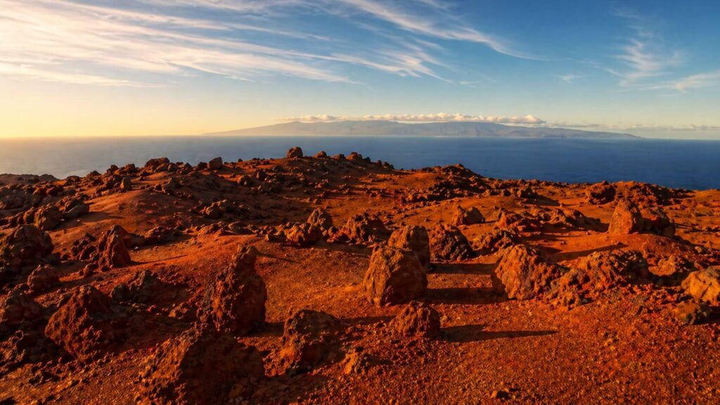 Paysage lunaire du Garden of the Gods à Lanai avec roches rouges et ocre au coucher du soleil, océan Pacifique et île de Molokai en arrière-plan